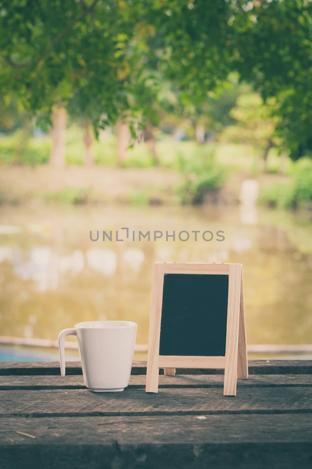 Small A-frame blackboard with blank area for text or message and coffee cup on rustic wood table in morning time with vintage filter effect