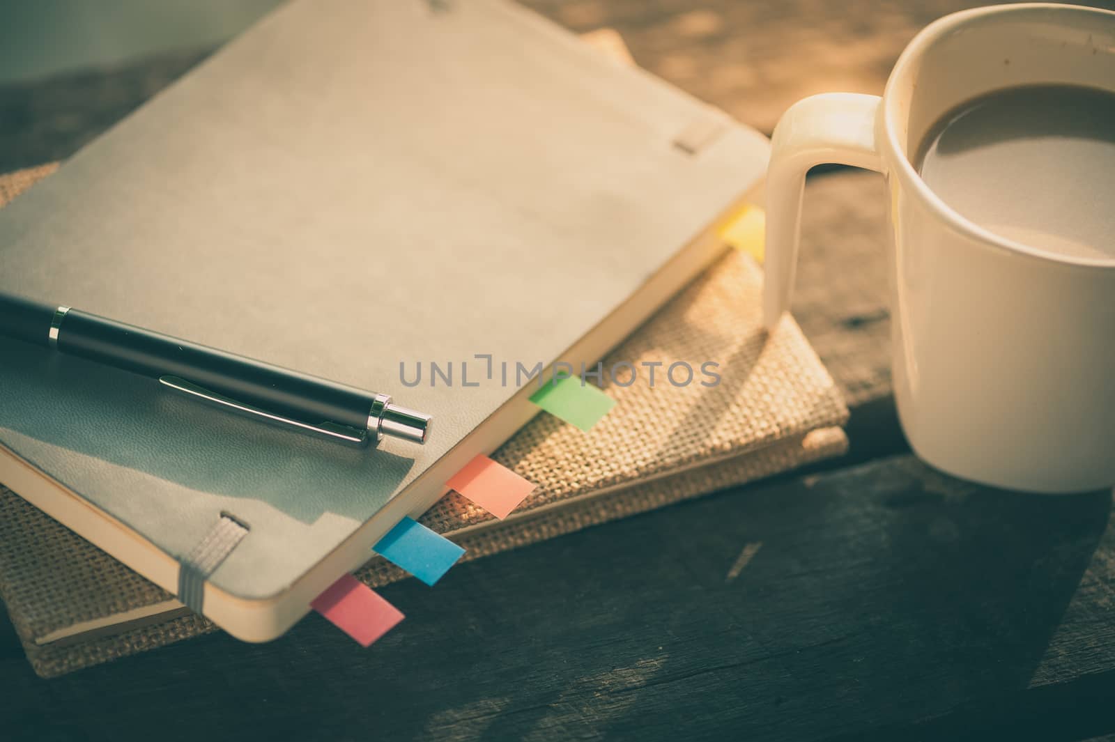 Pen, notebooks, and coffee cup on rustic wood table at outdoor area in morning time with vintage filter effect