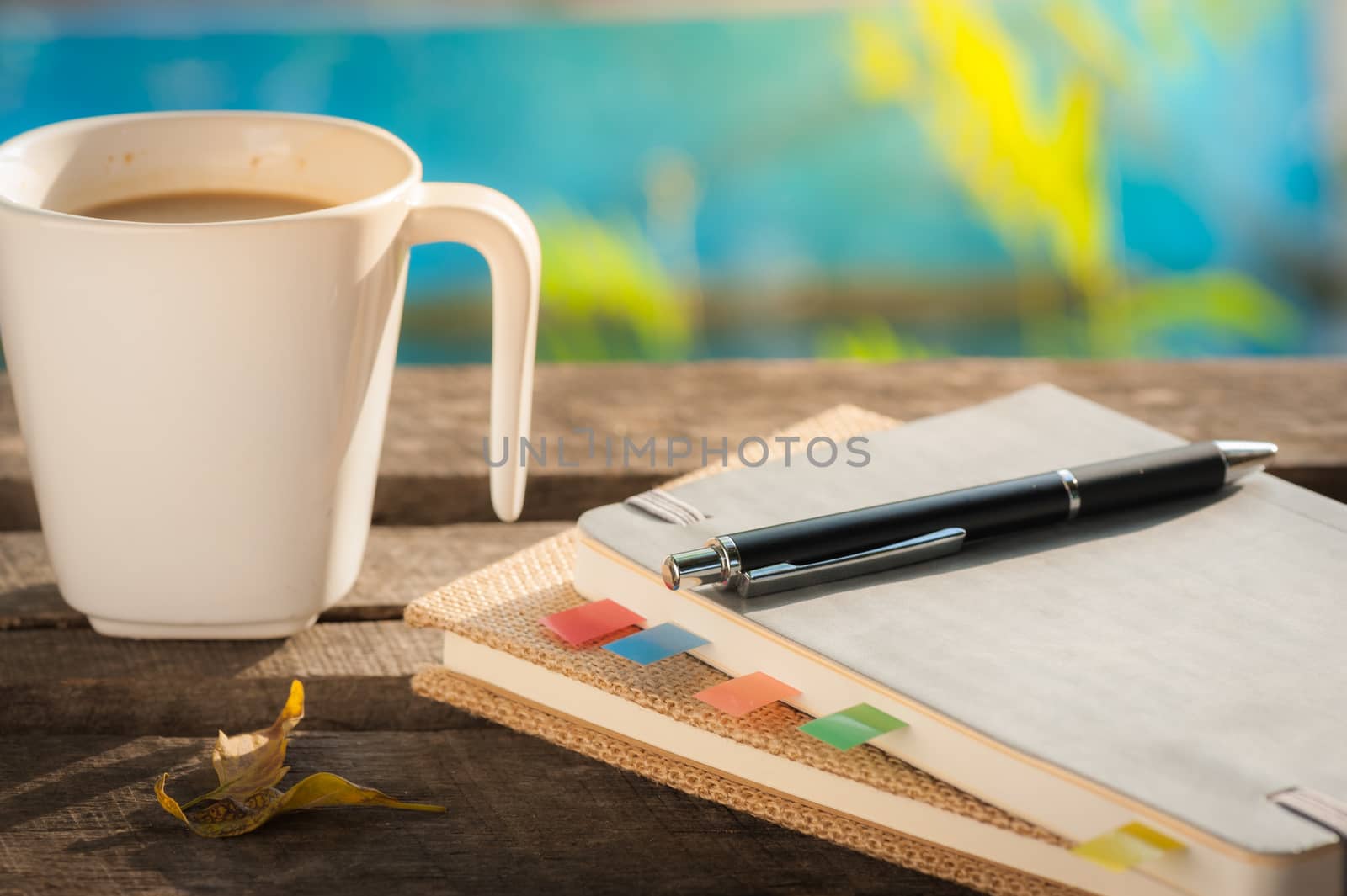Pen, notebooks, and coffee cup on rustic wood table at outdoor area in morning time