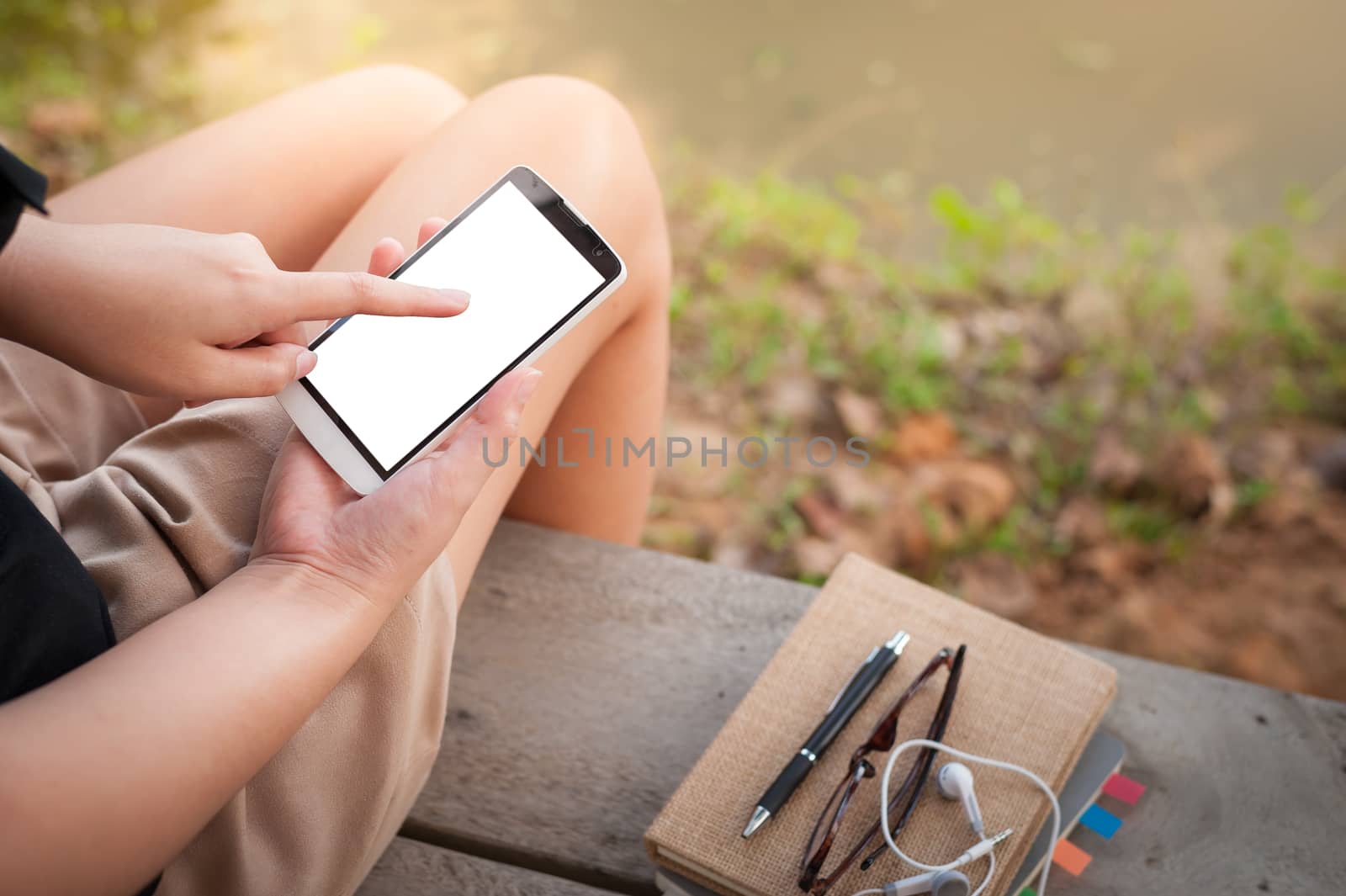 Young woman touching on smartphone blank screen while sitting on wood bench in park in morning time on weekend