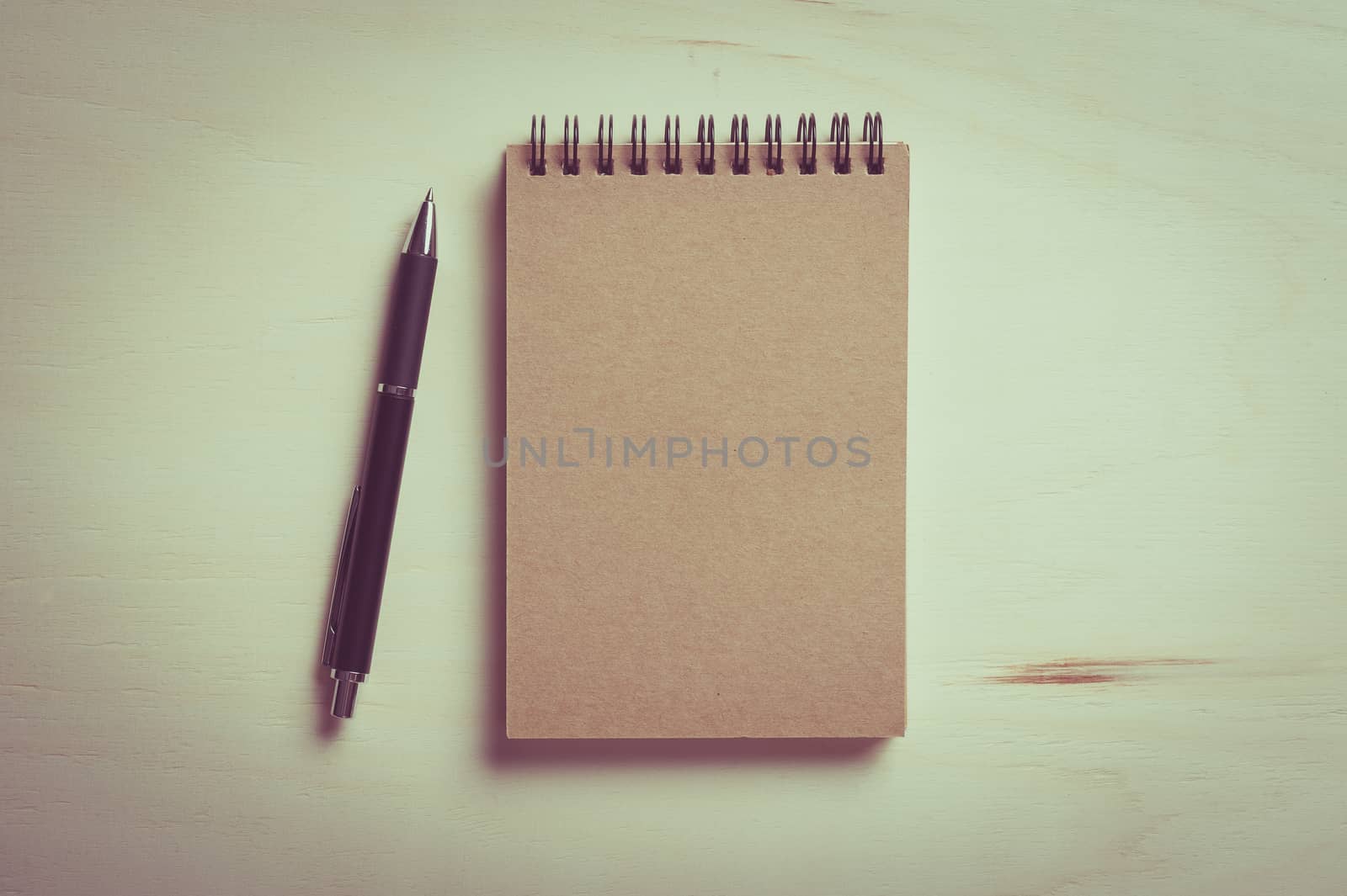 Closed notebook with blank area on front cover on wood table with vintage filter effect