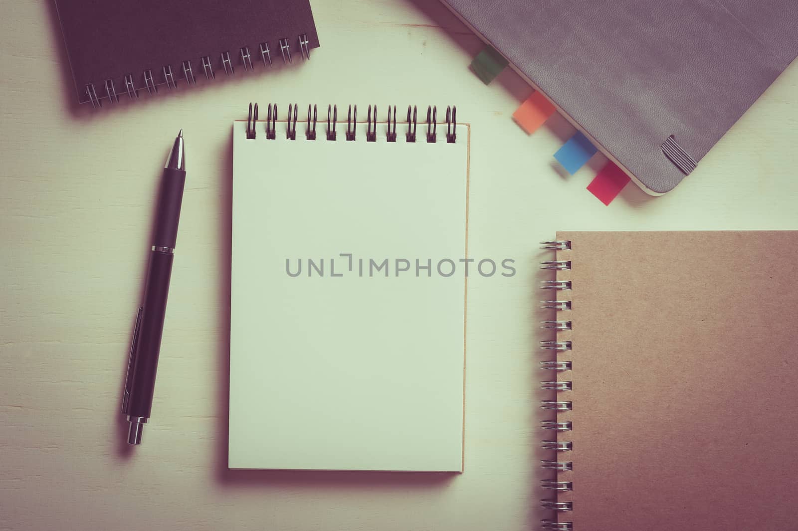 Opened notebook with blank area for text or message, grey, blank, and brown closed notebook on wood table with vintage filter effect