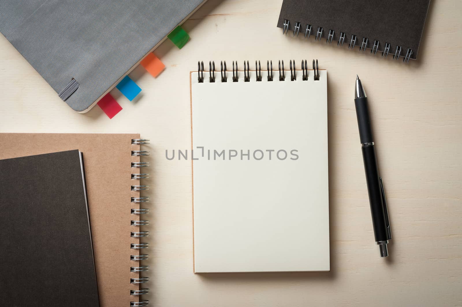 Opened notebook with blank area for text or message, grey, blank, and brown closed notebook on wood table