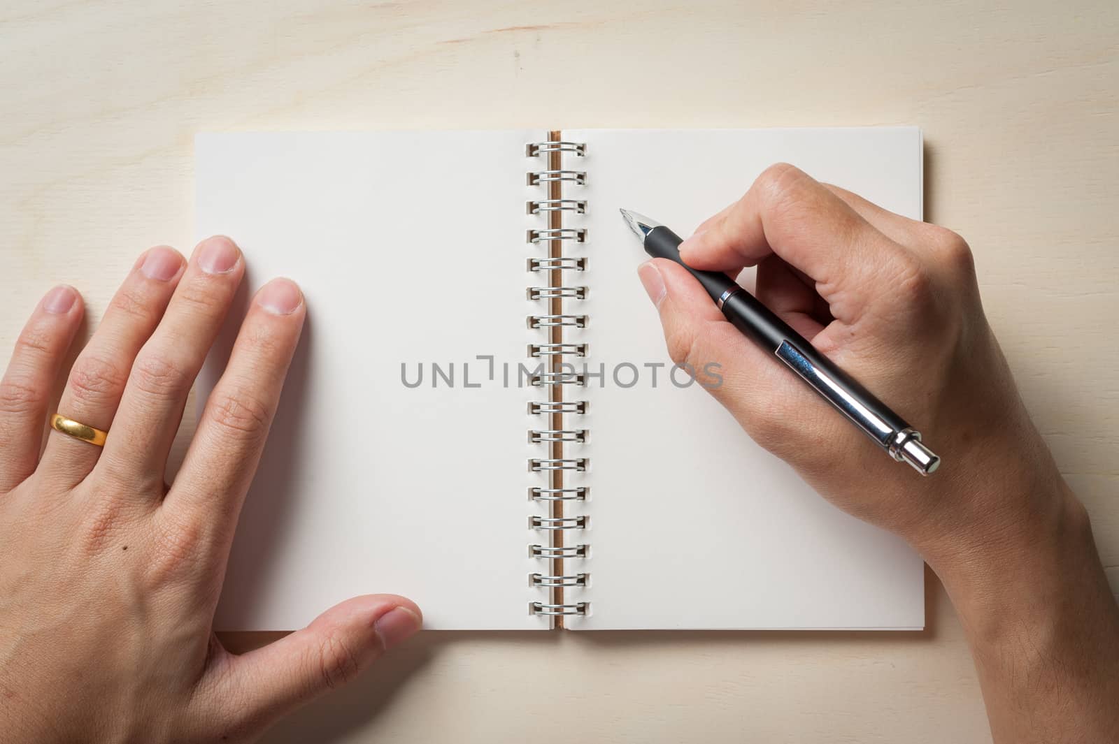 Male right hand writing on opened notebook with blank area for text or message and pen on wood table in morning time