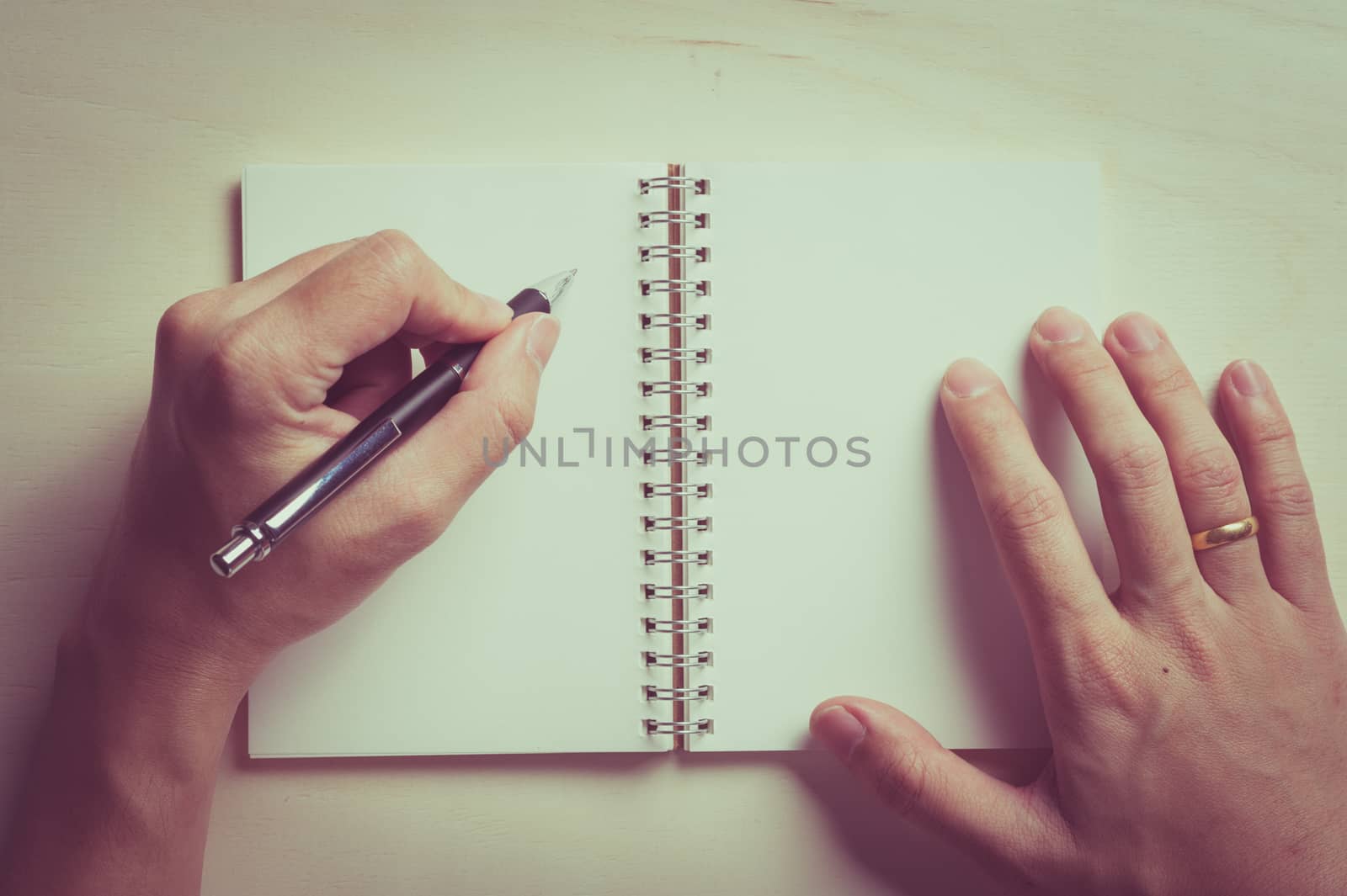 Male left hand writing on opened notebook with blank area for text or message and pen on wood table with vintage filter effect
