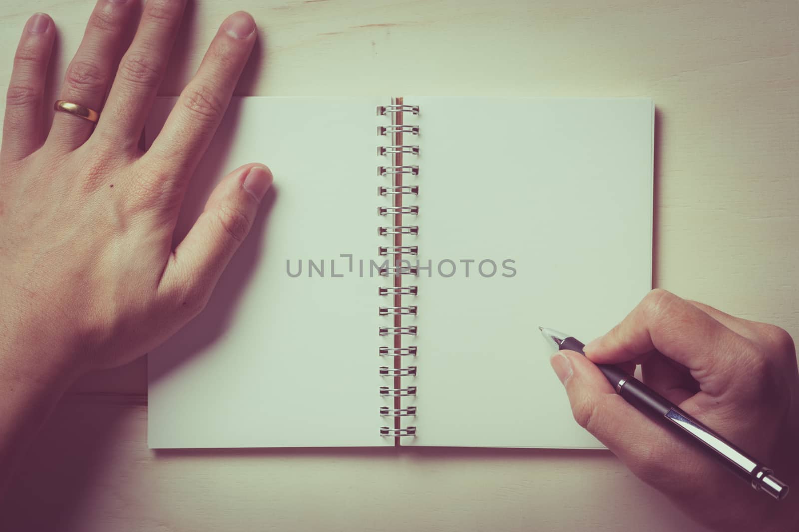 Male right hand writing on opened notebook with blank area for text or message and pen on wood table with vintage filter effect