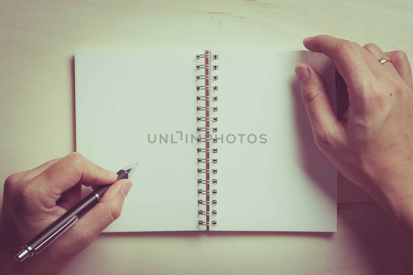 Male left hand writing on opened notebook with blank area for text or message and pen on wood table with vintage filter effect