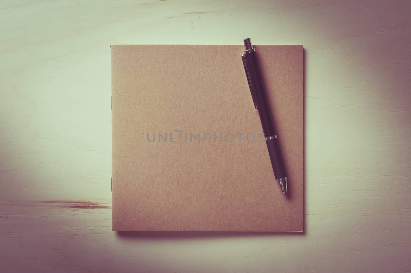 Closed sketch book with blank area on front cover on wood table with vintage filter effect