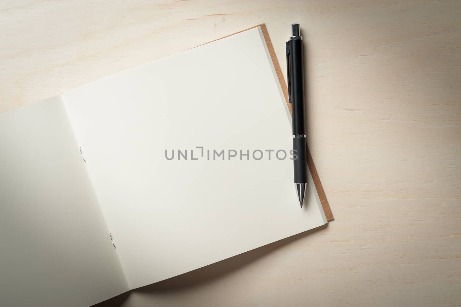 Opened sketch book with blank area for text or message and pen on wood table in morning time with low key scene