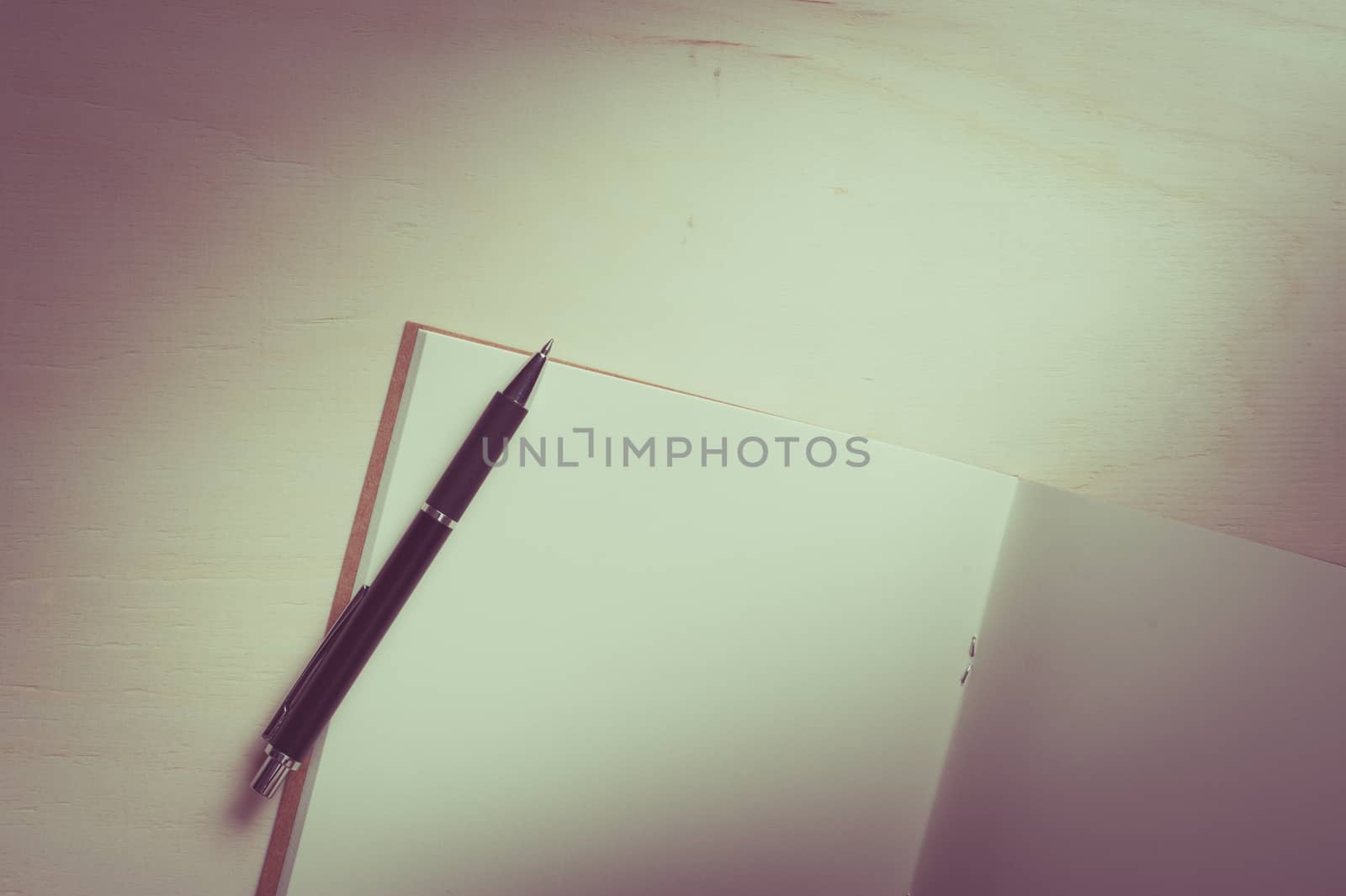 Opened sketch book with blank area for text or message and pen on wood table with vintage filter effect