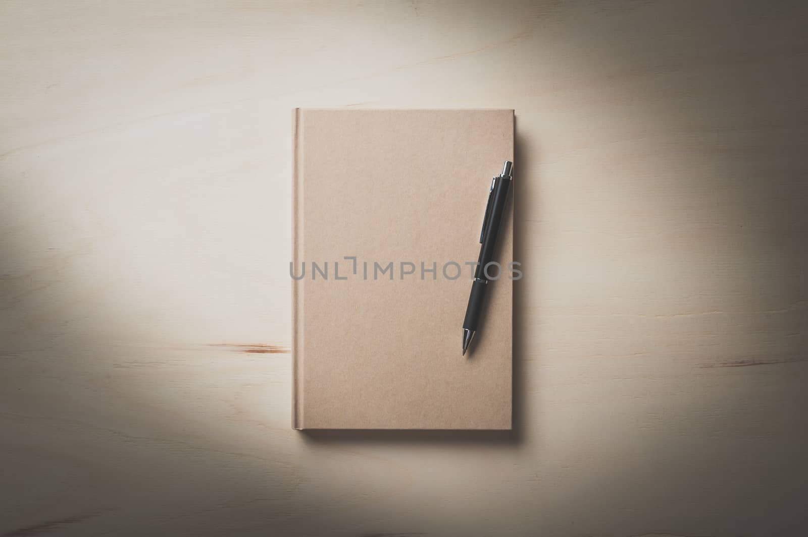 Closed hard cover notebook with blank area on front cover on wood table in morning time with film filter effect