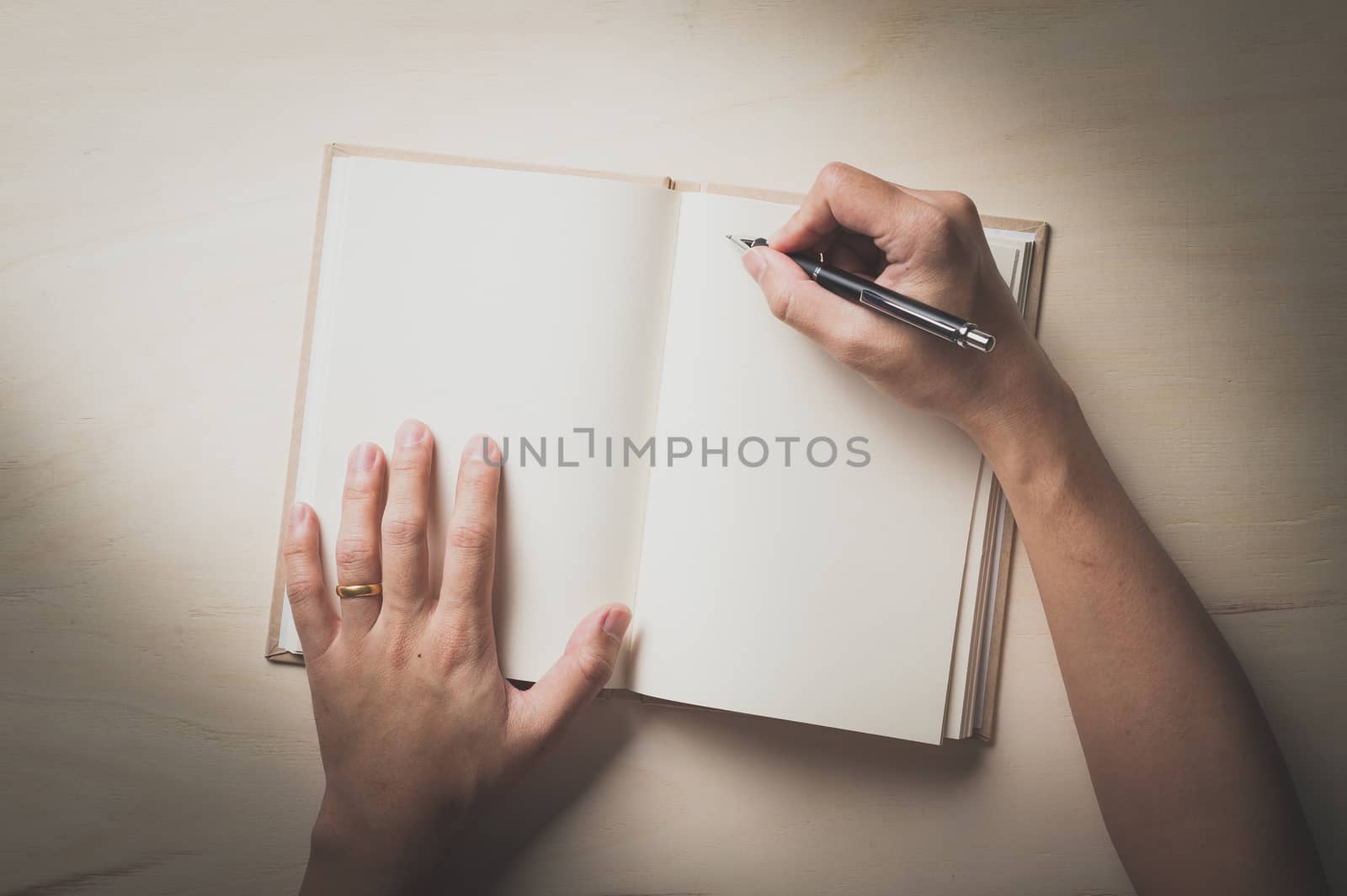 Male right hand writing on opened notebook on wood table in morning time with film filter effect