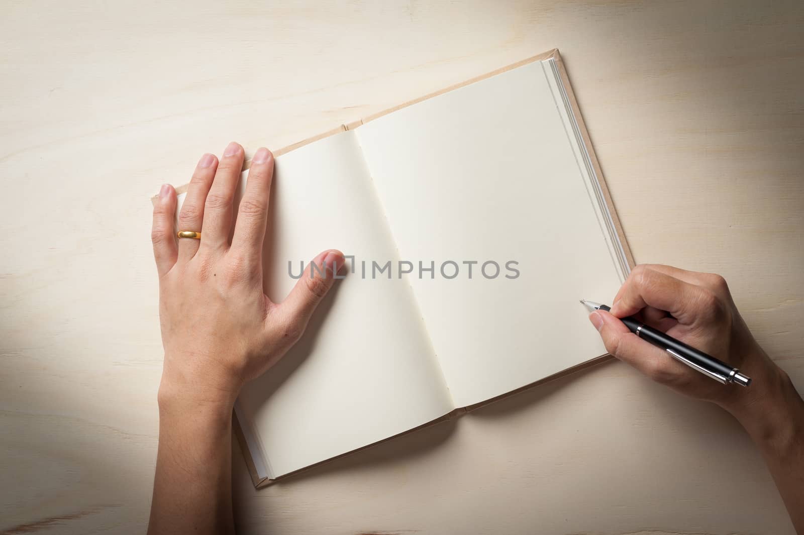 Male right hand writing on opened notebook on wood table in morning time with low key scene