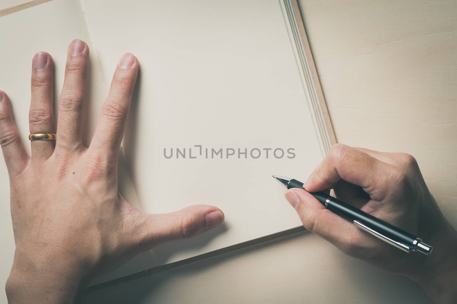 Male right hand writing on opened notebook on wood table in morning time with vintage filter effect