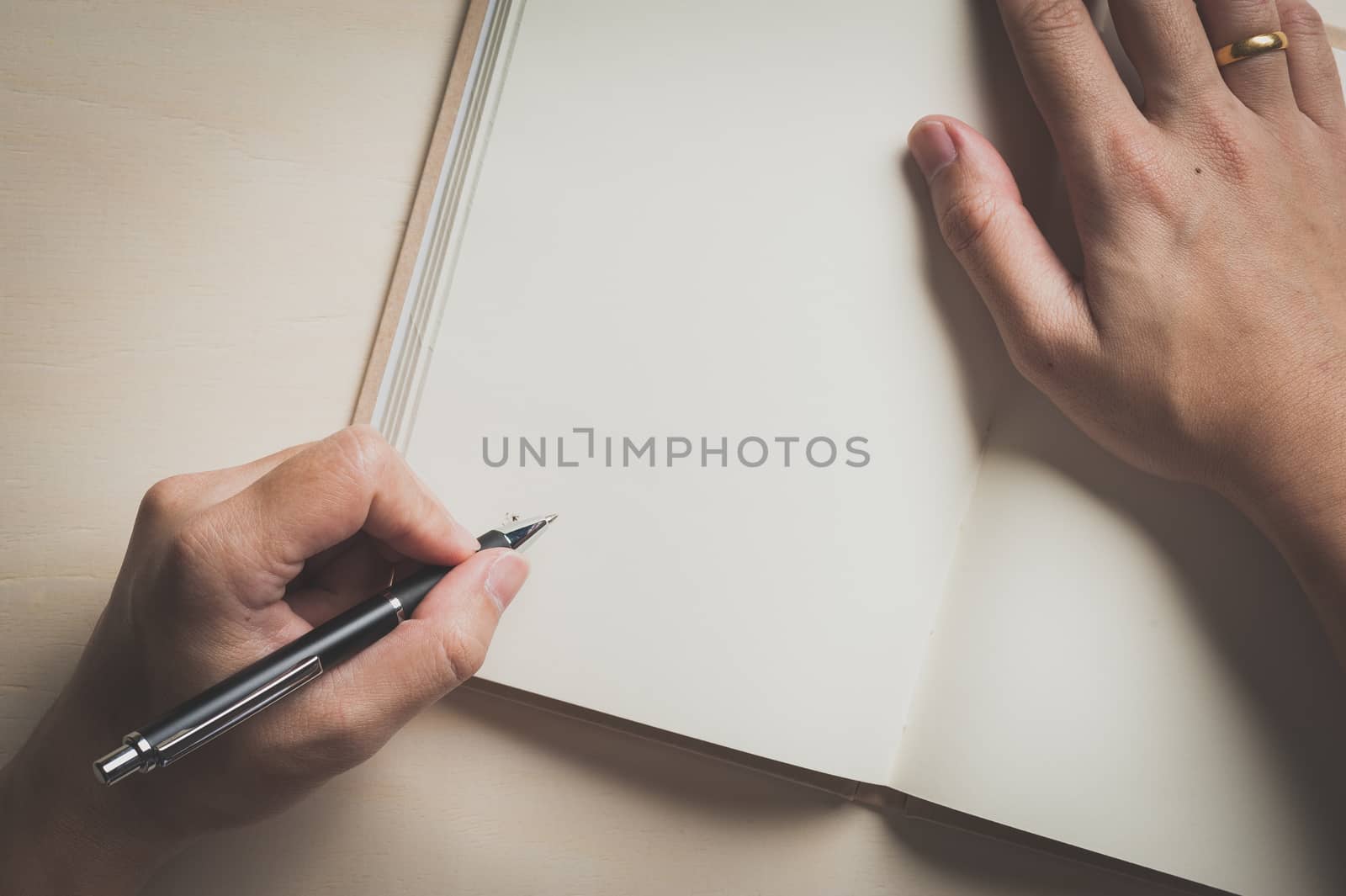Male left hand writing on opened notebook on wood table with vintage filter effect