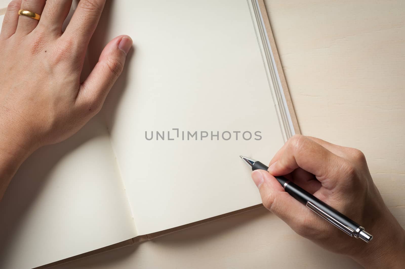 Male right hand writing on opened notebook on wood table in morning time with low key scene