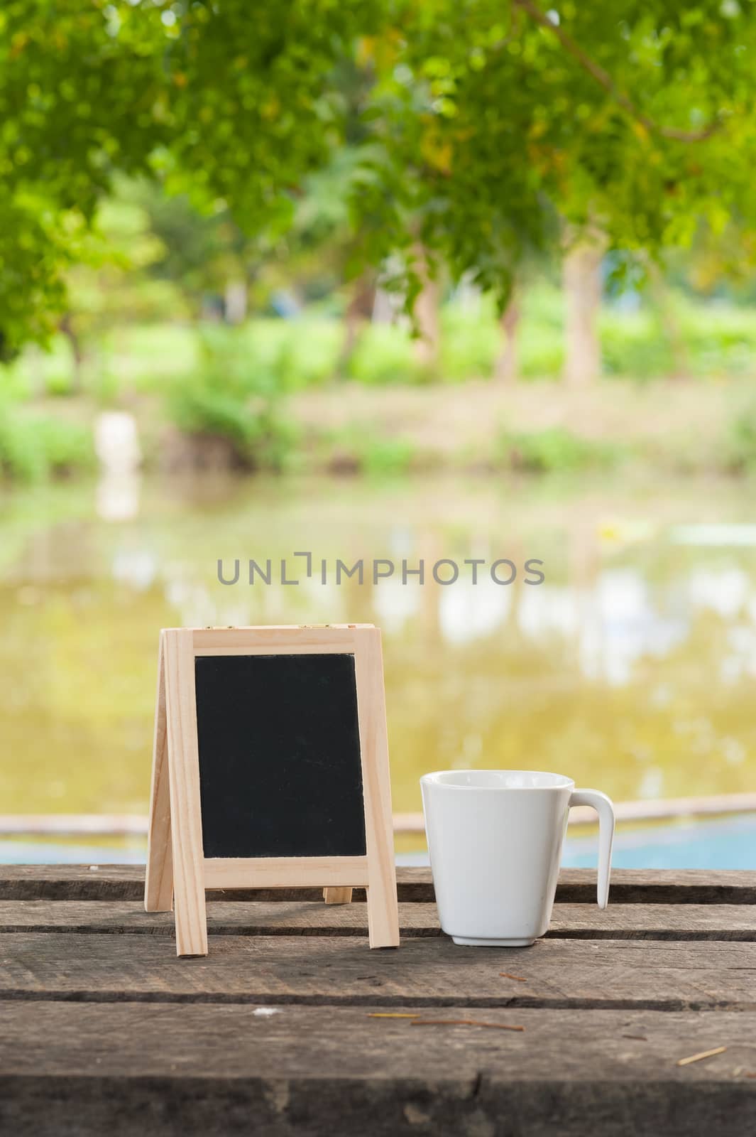 Small A-frame blackboard with blank area for text or message and coffee cup on rustic wood table in morning time