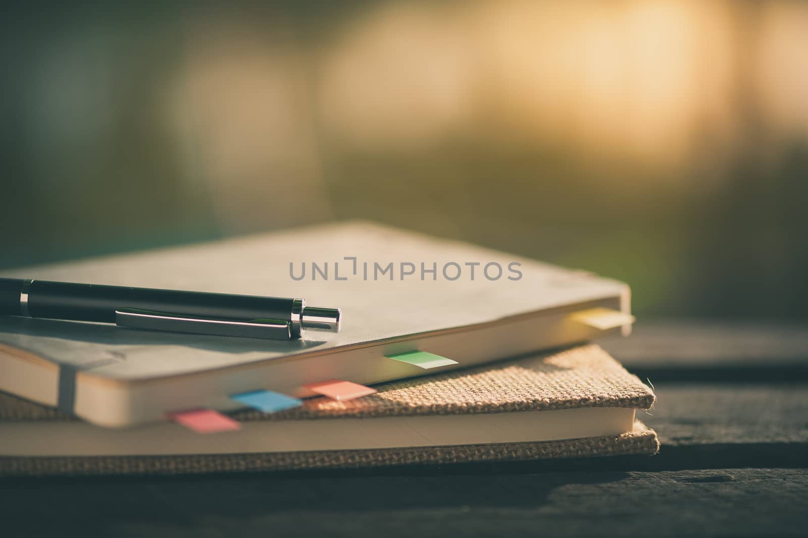 Pen and notebooks on rustic wood table at outdoor area with morning time on summer with vintage filter effect