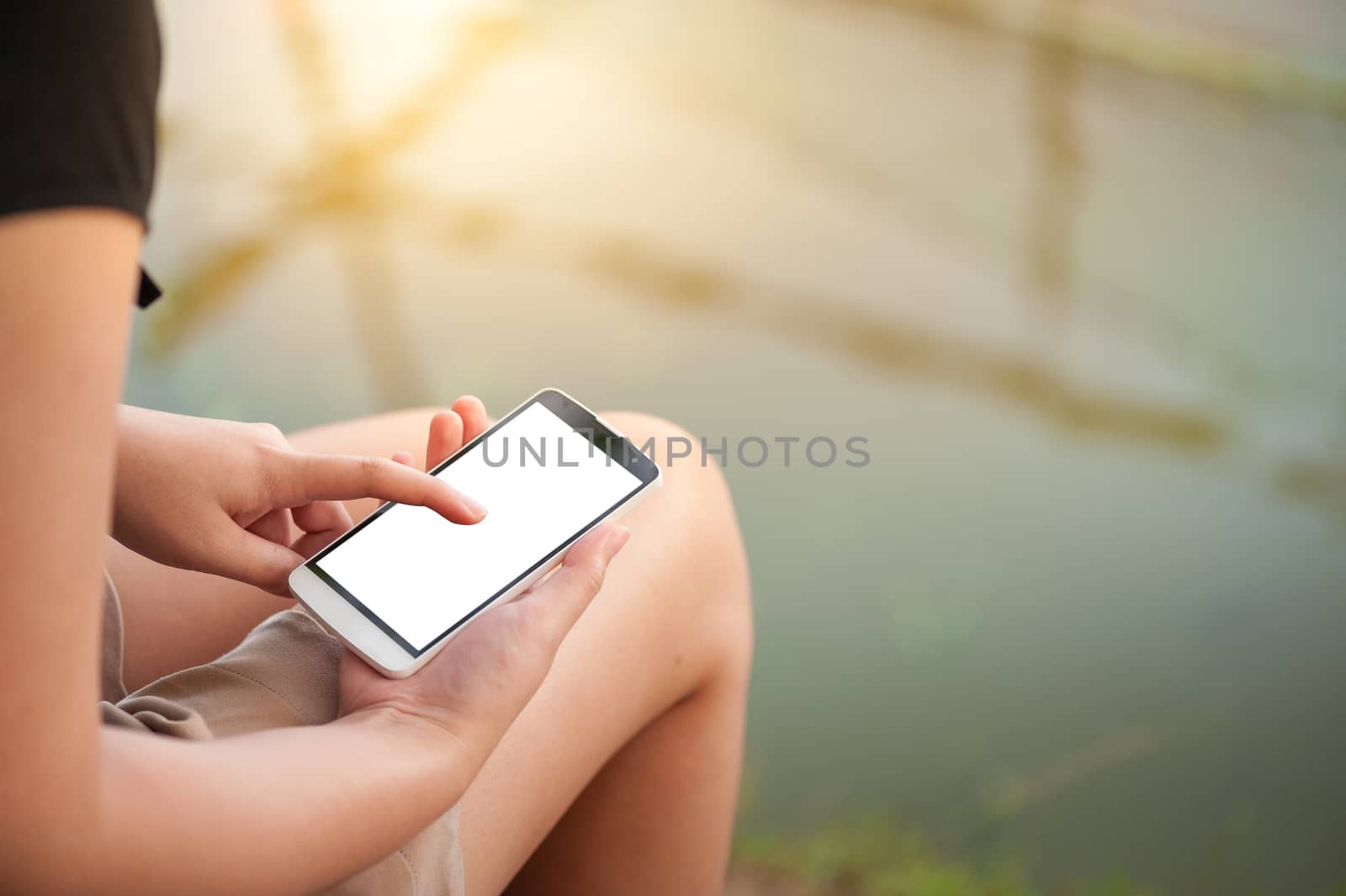 Young woman touching on smartphone blank screen while sitting in park in morning time on weekend