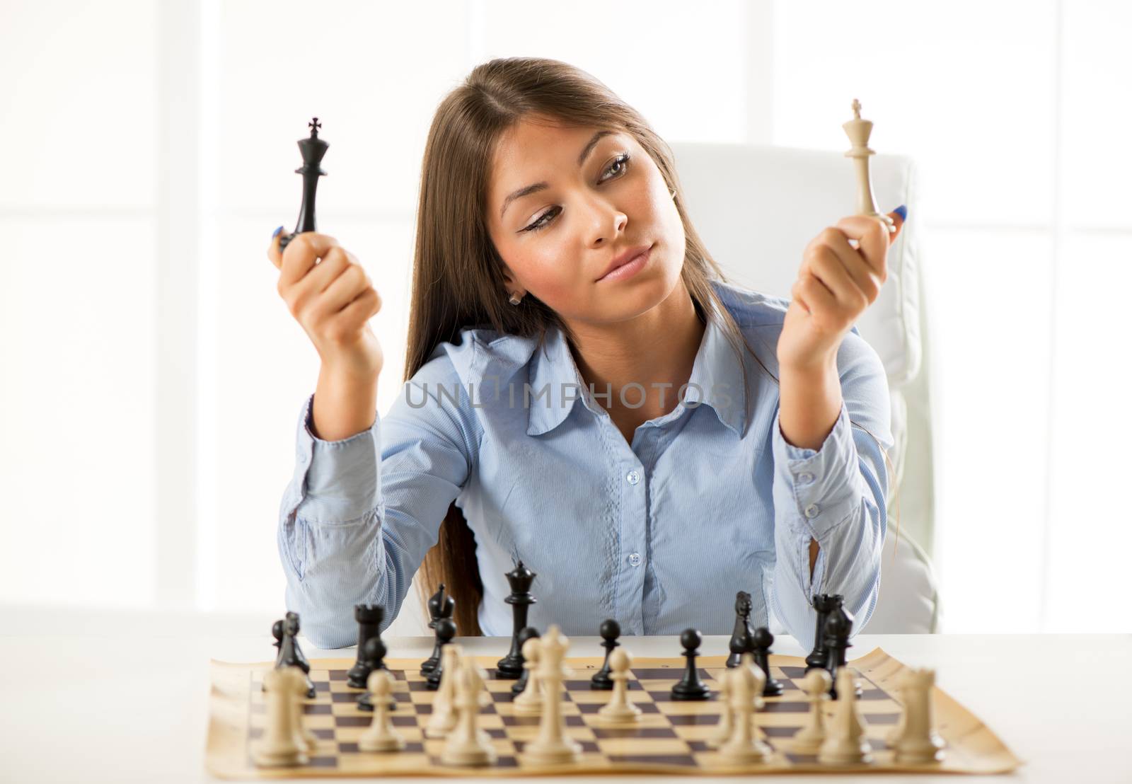 Young beautiful businesswoman devises Business strategy. She sitting above the chessboard with figures and thinking.