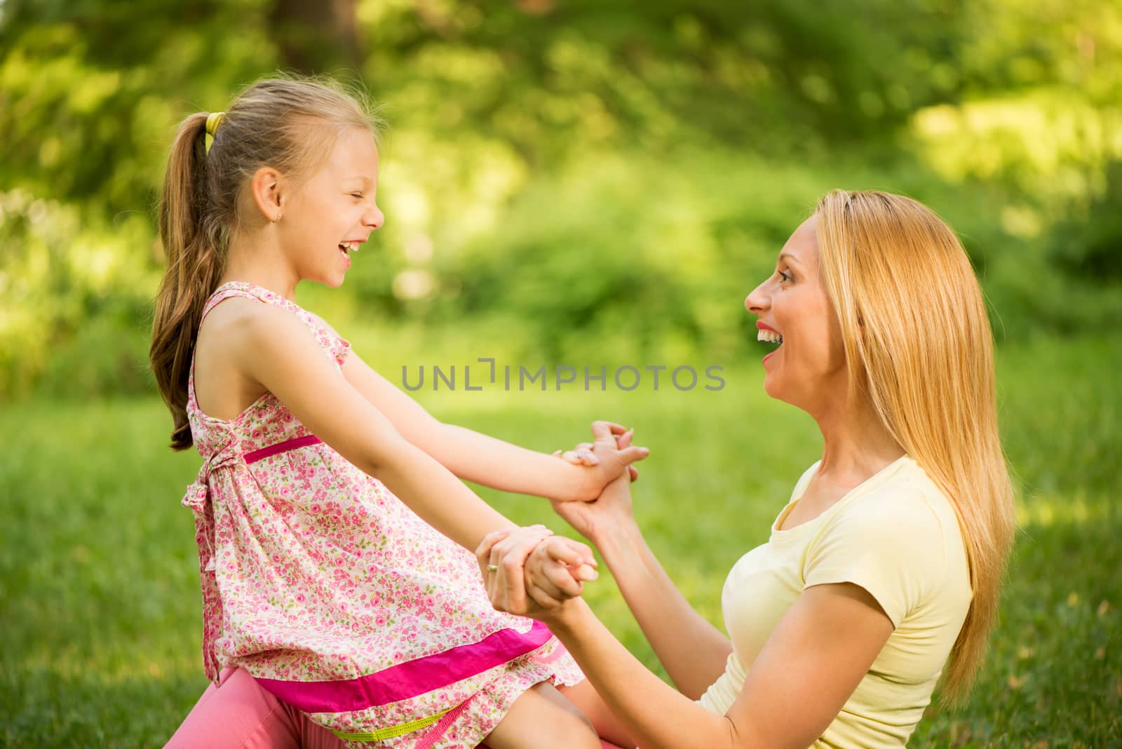 Happy cute little girl sitting on mother's lap in the park