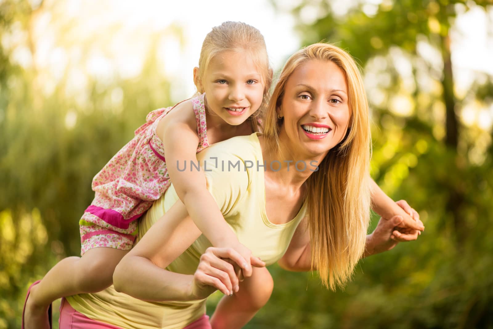 Beautiful mother giving her cute little girl piggyback and smiling in the park