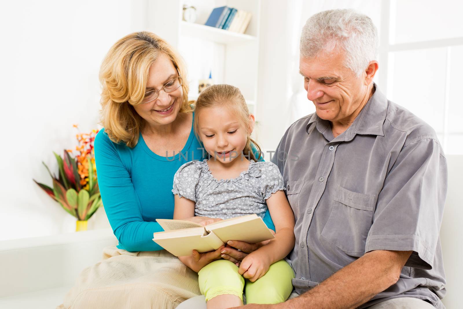 Grandparents with little girl reading book at home