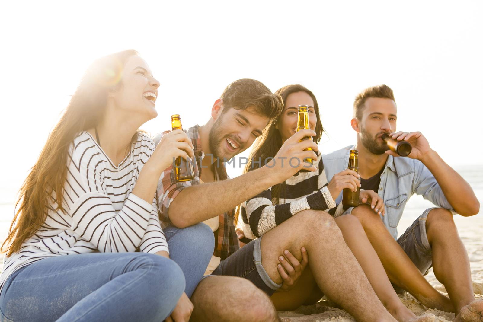 Friends having fun together at the beach and drinking a cold beer