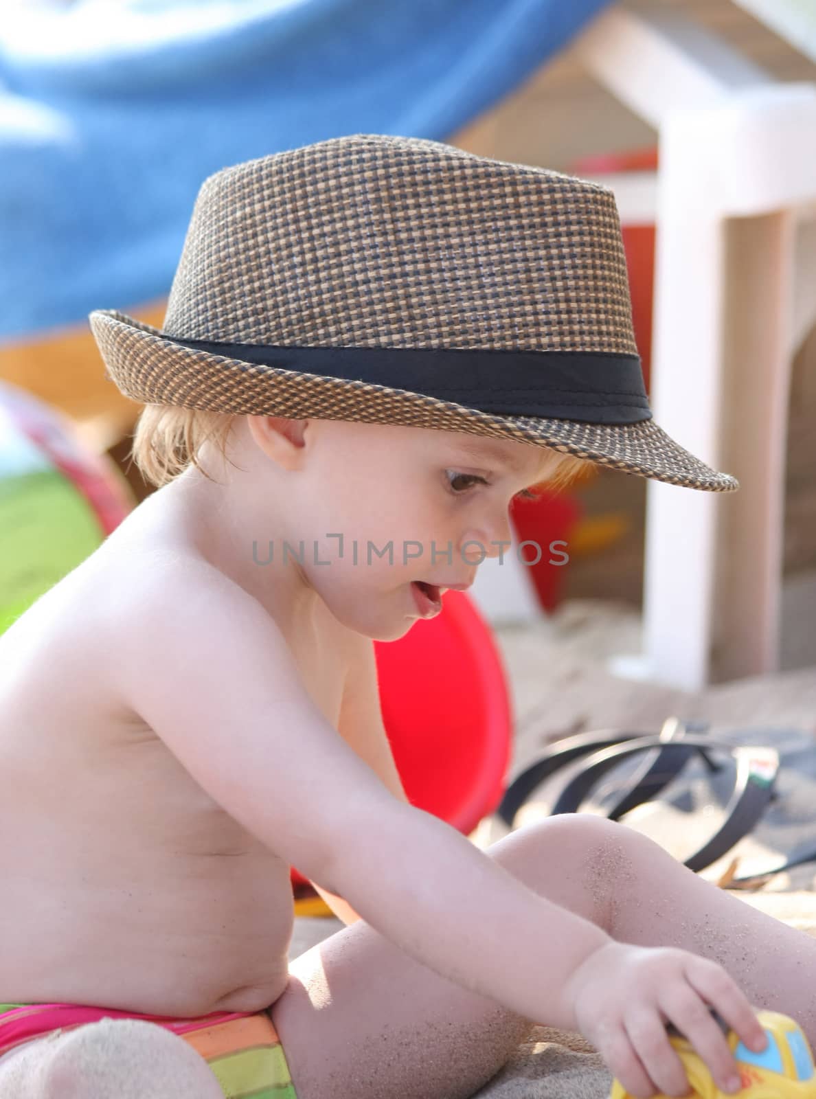 Baby girl with big hat playing on the beach