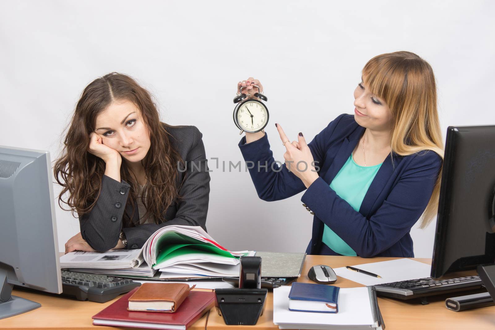  Office workers at the end of the day, one with a smile indicates a clock, another weary head props