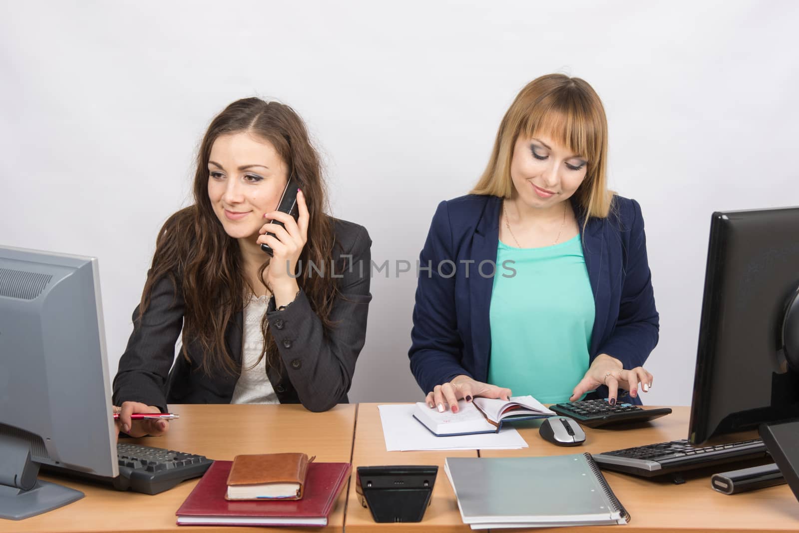  Office colleagues girl sitting behind a desk, with a phone, the other with a calculator