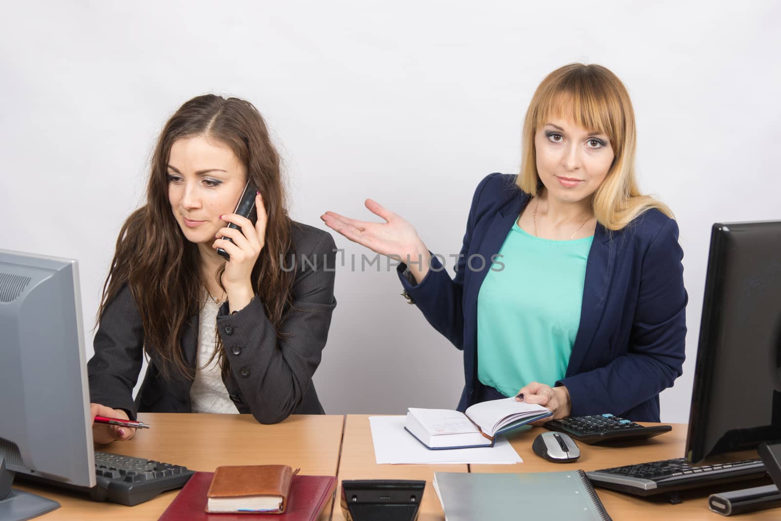 The girl in the office puzzled indicates colleague talking on the phone by Madhourse