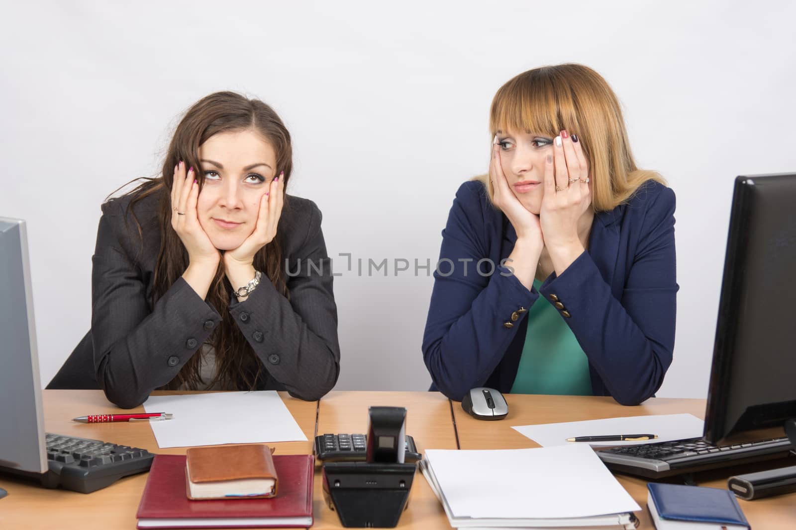 Two office workers tired tortured sitting behind a desk