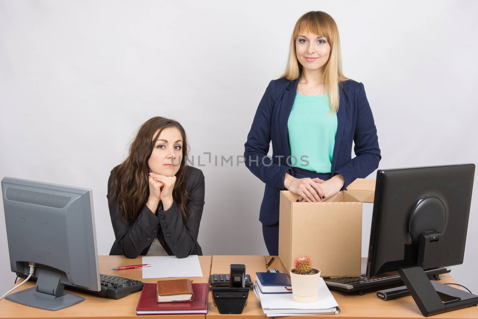 The girl in the office is facing the box with things near the colleague sitting next