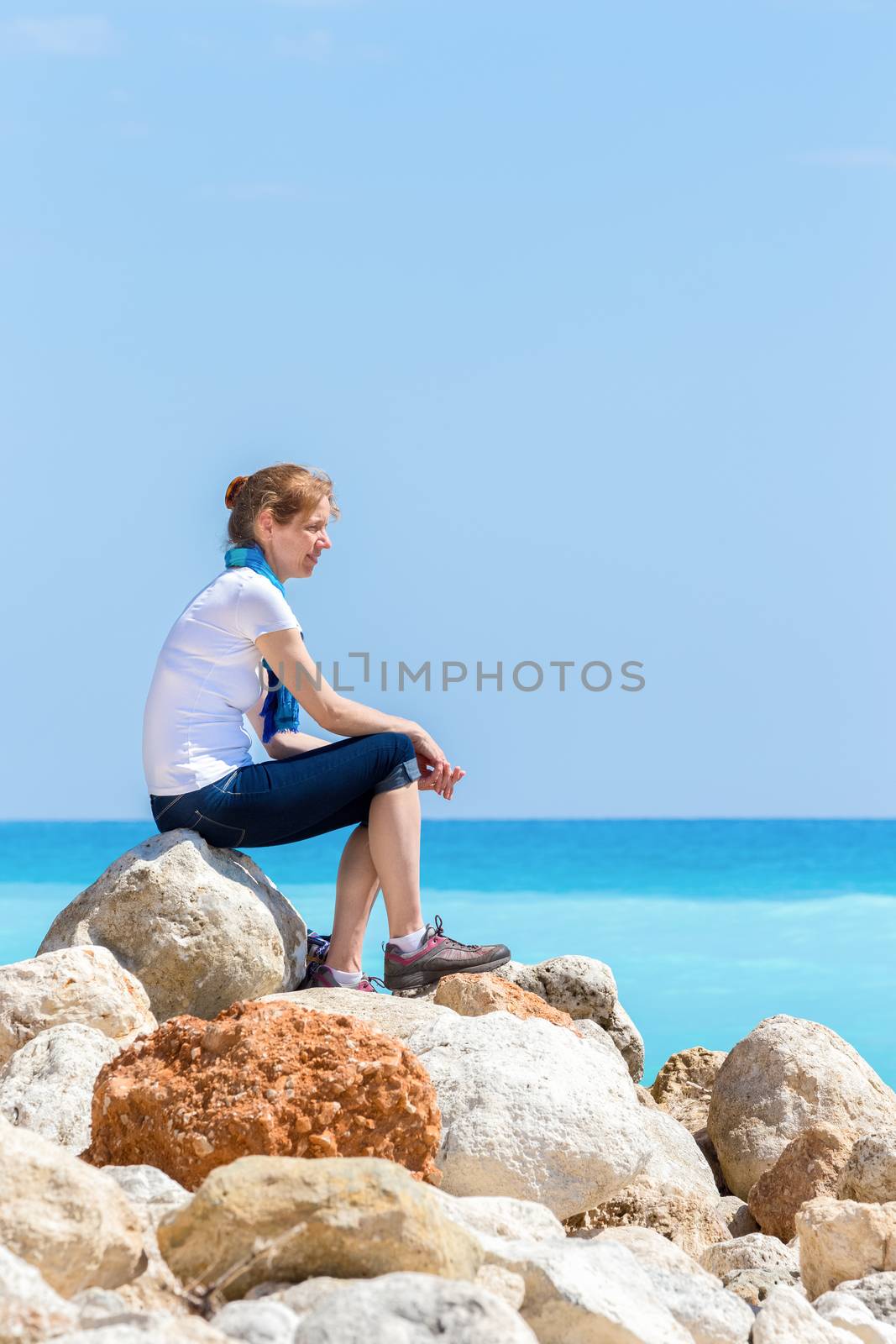 European woman sitting on rocks at coast near sea