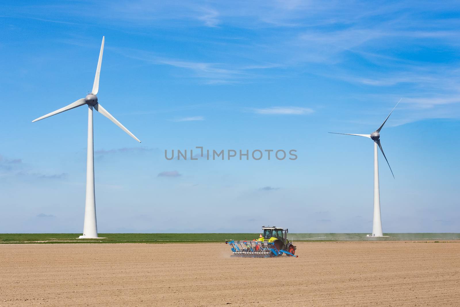 Farmer on tractor sowing in soil near dike and two windmills in the netherlands