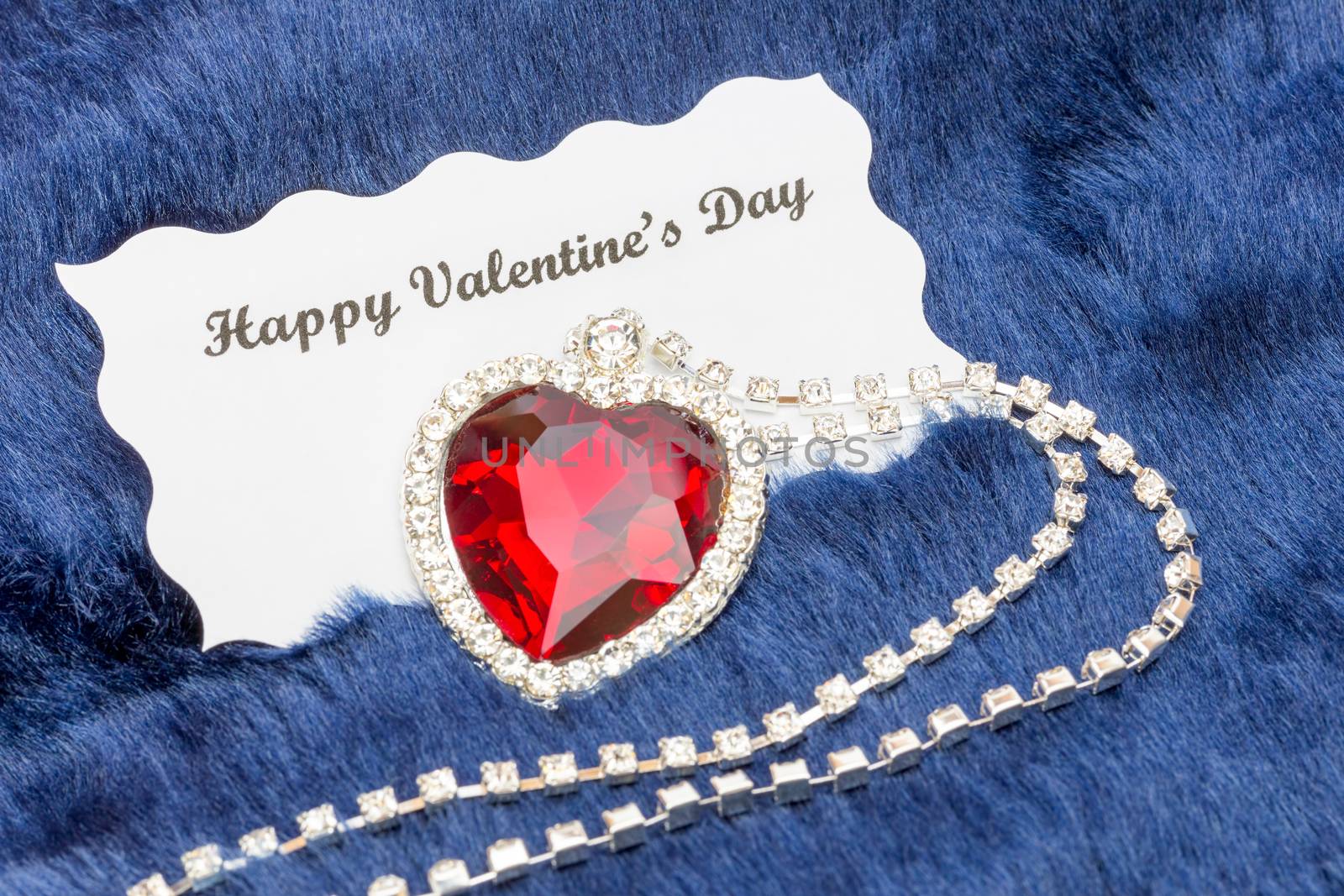 Red jewelry necklace with message on Valentine's card isolated on blue cloth background
