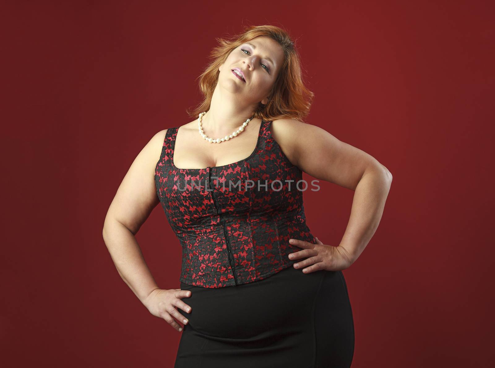 forty year old woman with red hair, wearing a red corset against a red background