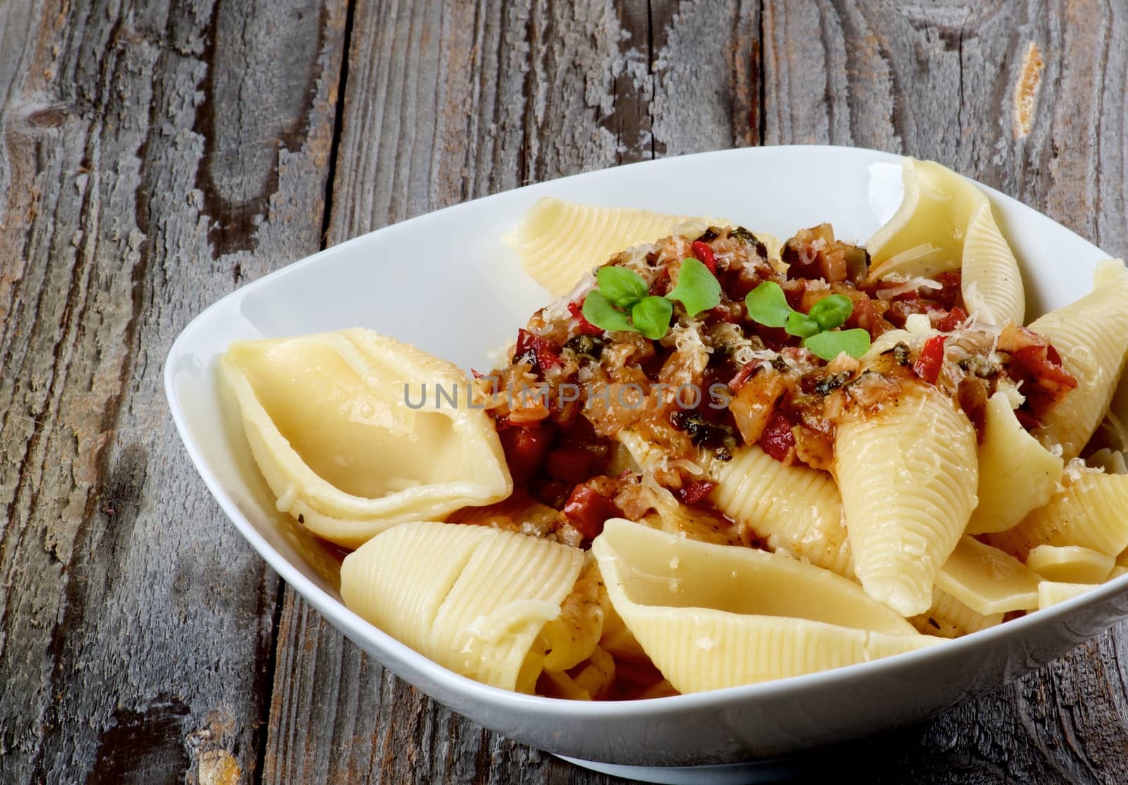 Delicious Conchiglie Giganti Pasta (Giant Pasta Shells) with Meat Sauce Bolognese in White Bowl closeup on Rustic Wooden background