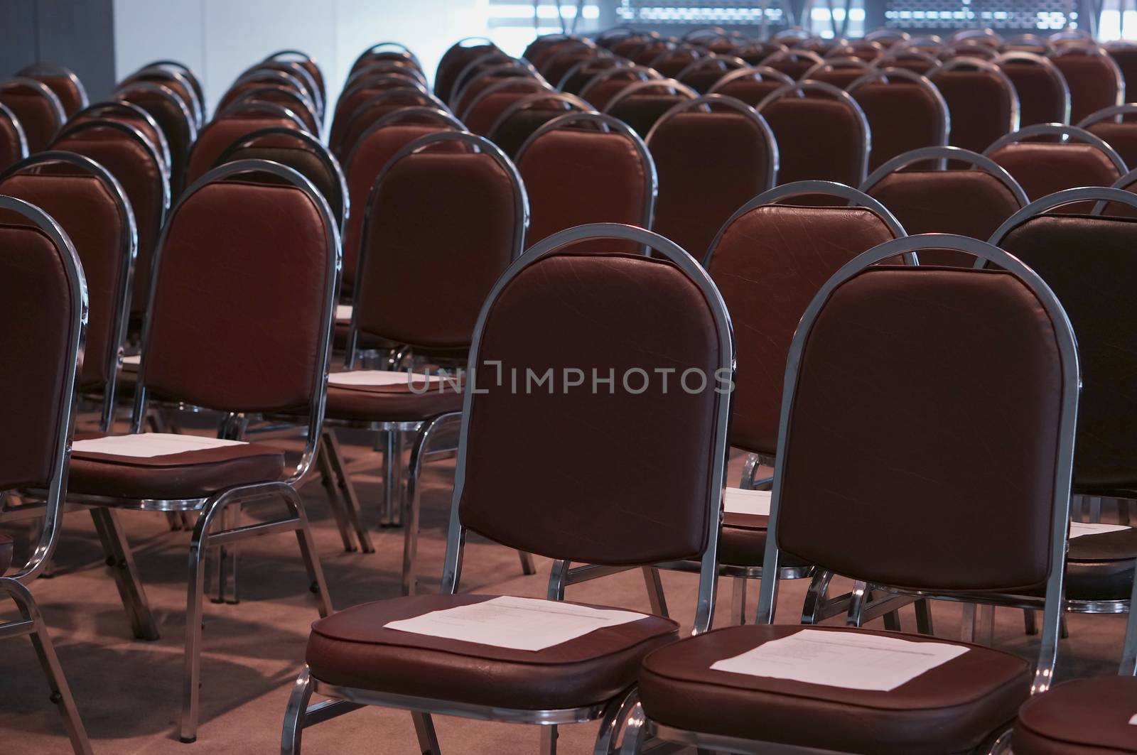 Empty classroom contained with brown chairs and document on top.