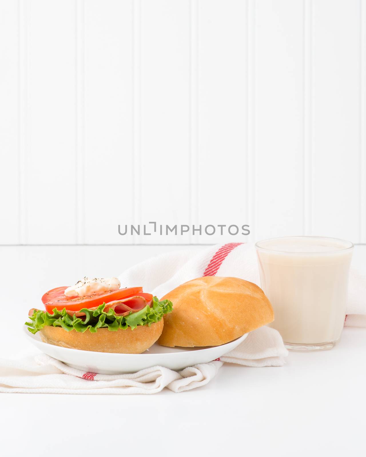 Ham and tomato sandwich on a fresh kaiser bun served with cold milk.