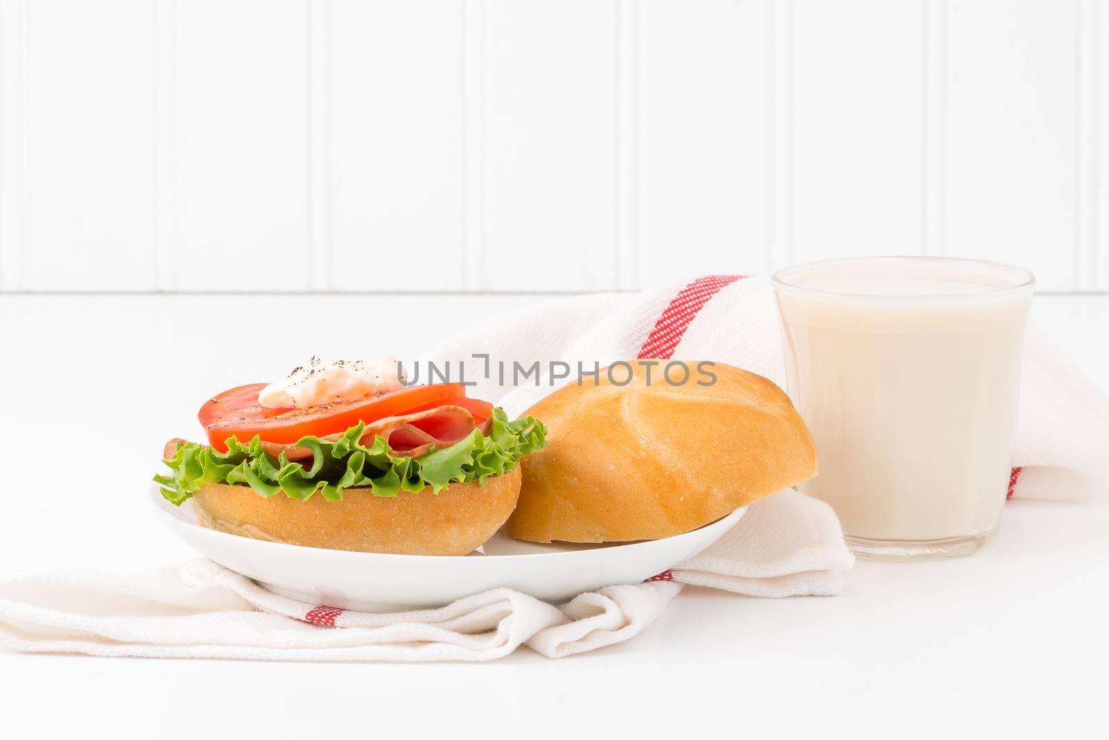 Tomato and ham sandwich on a fresh kaiser bun served with a glass of cold milk.