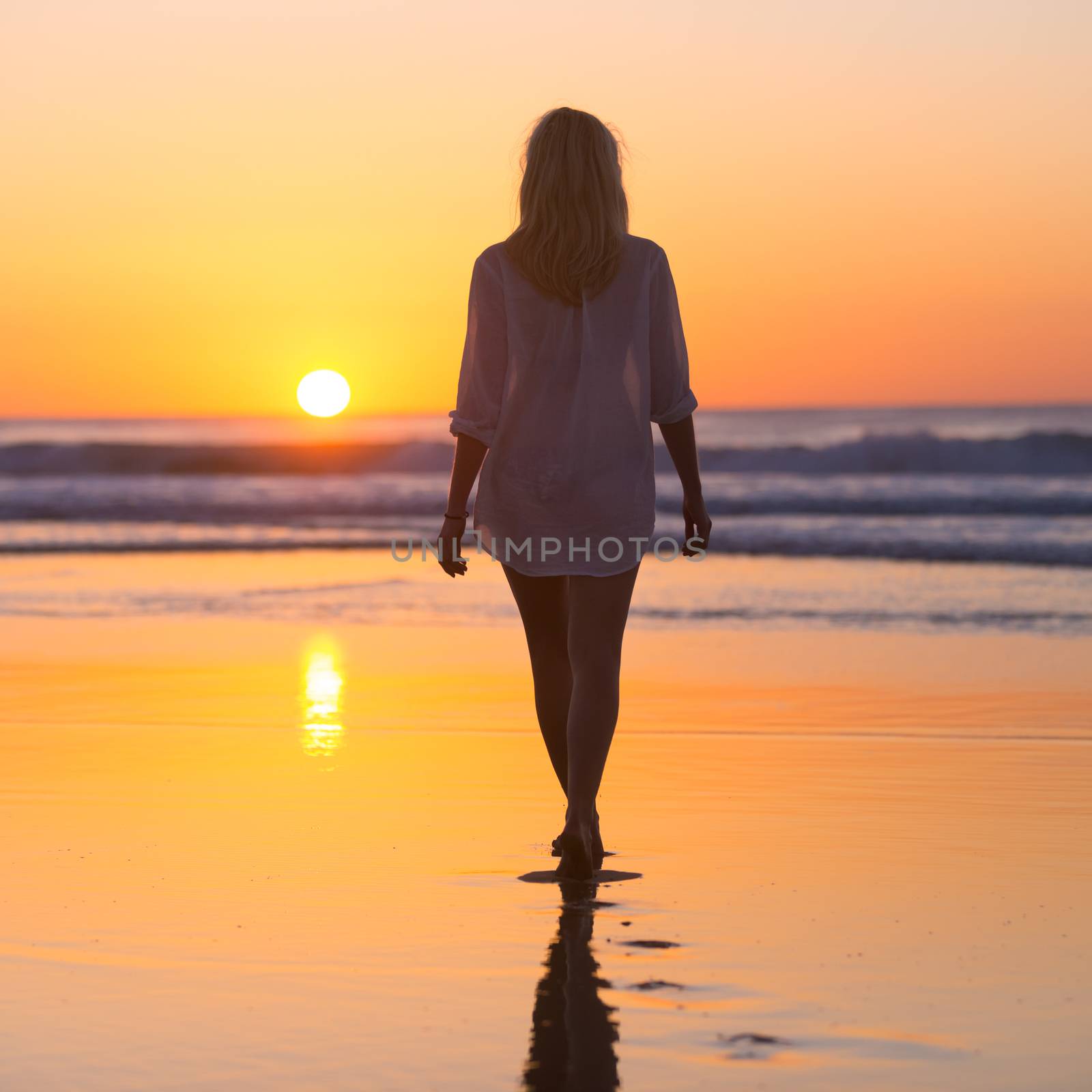 Lady walking on sandy beach in sunset. by kasto