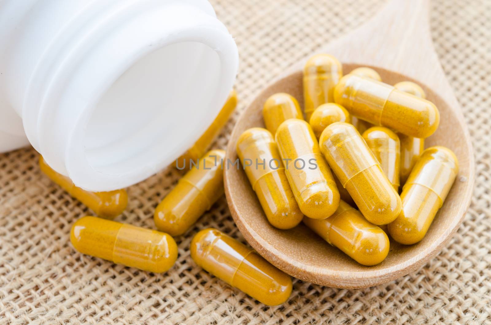 Herbal capsule spill out from bottle on sack background.