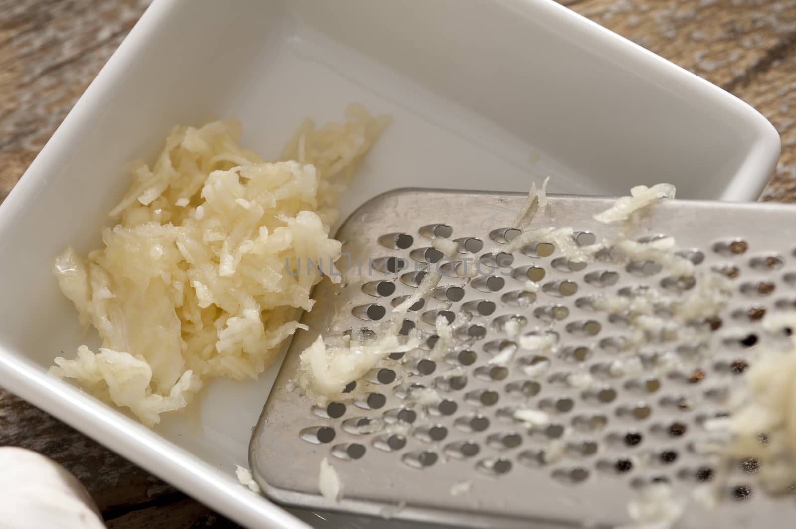 Grated fresh garlic in a small rectangular dish with a stainless steel grater at the side, high angle view