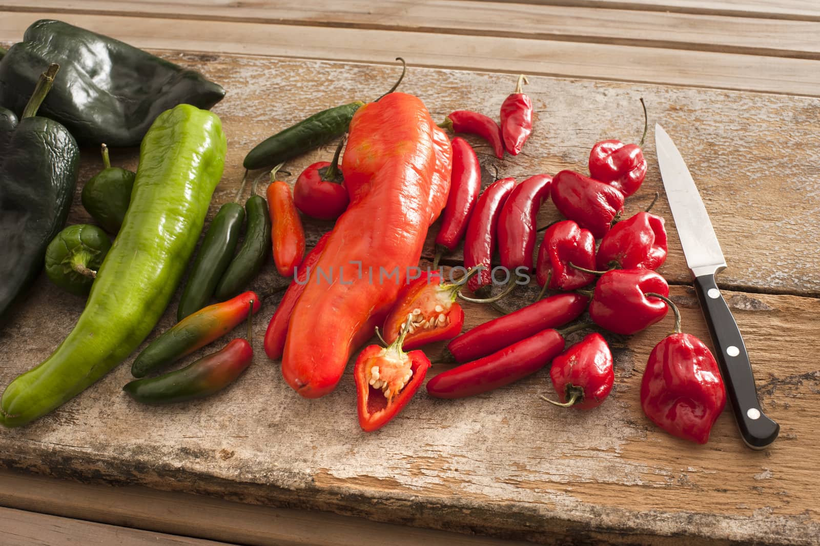 Assortment of colorful fresh red and green spicy chili peppers on an old rustic wooden table with a kitchen knife