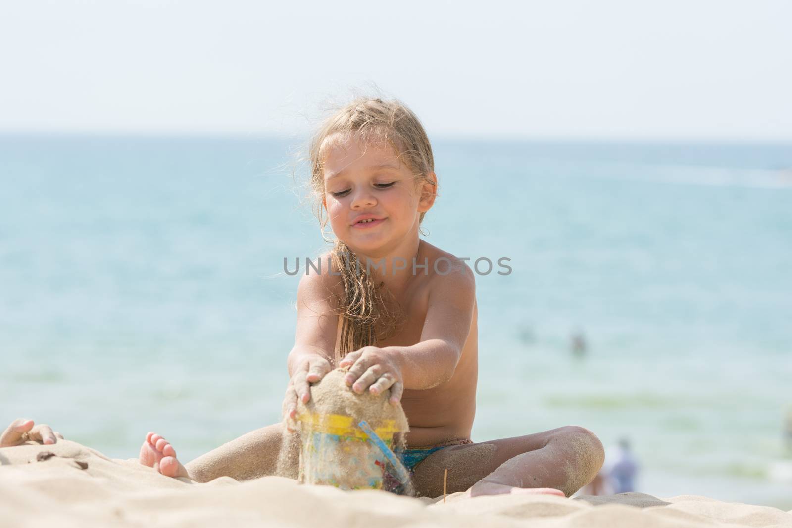 Pretty girls four years playing in the sand with a child on the sea beach bucket