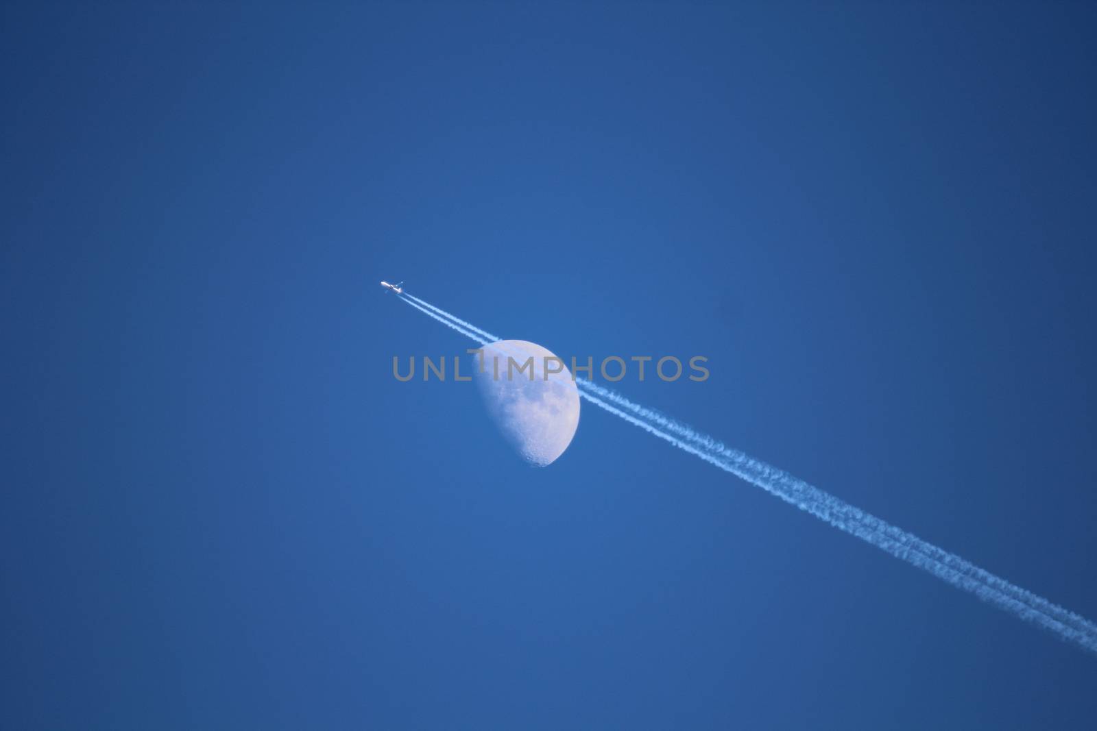 Jet airplane with trail of fuel on blue sky and big moon