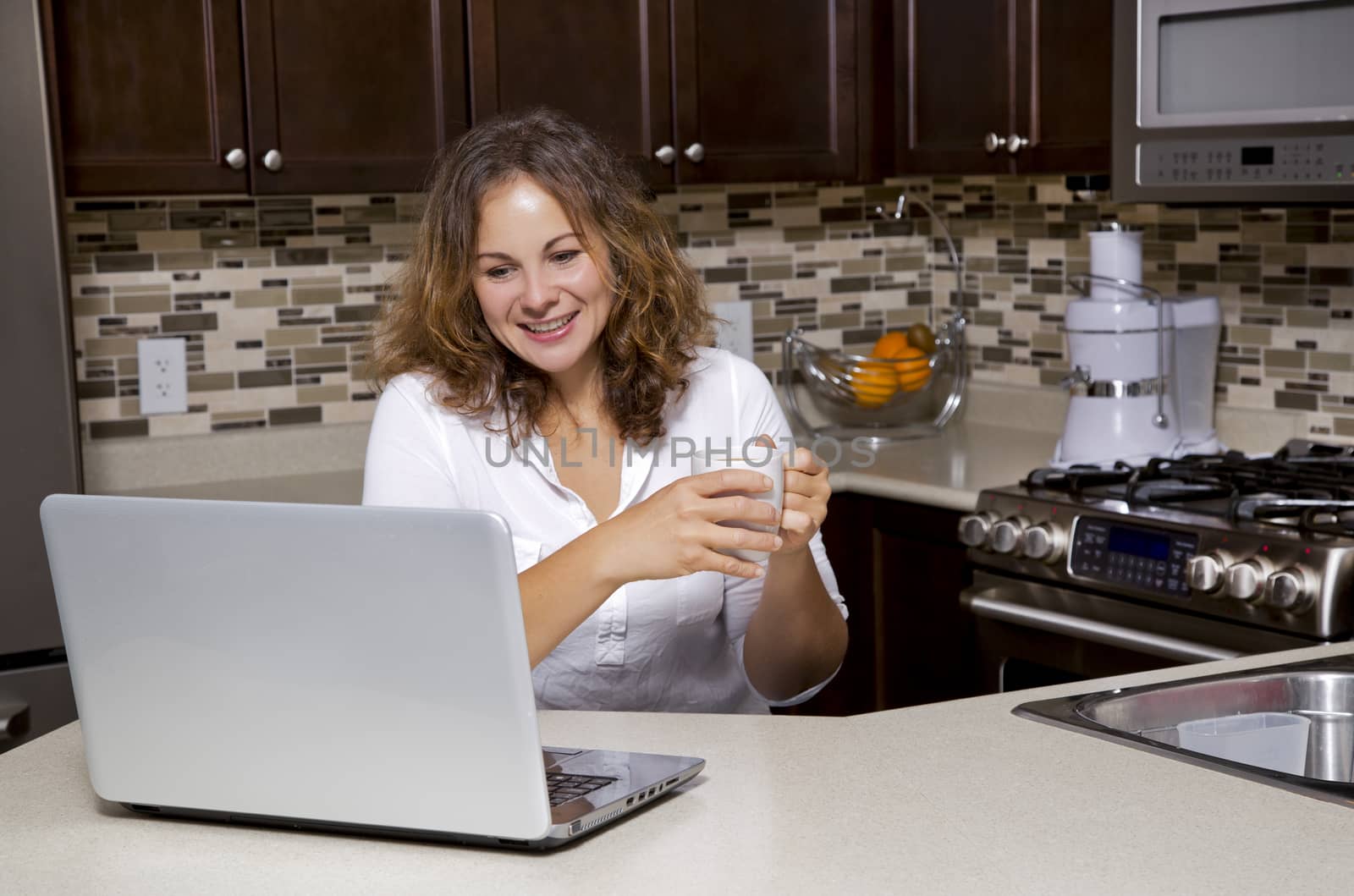 woman drinking coffee while working on ther laptop in the kitchen