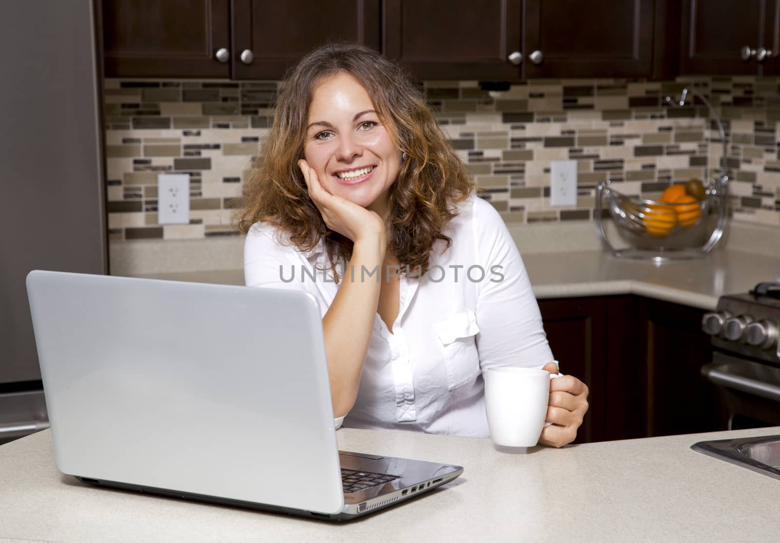 woman drinking coffee while working on the laptop in the kitchen